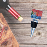Metal wine bottle stopper topped with a square tile painted with Muskegon Lighthouse scene in red sky, blue water, and white lighthouse next to house with trees.