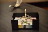 Silver branch-shaped napkin holder resting on colorful patterned napkins inside a rectangular black tray on a dark wood table.