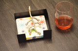 Silver branch-shaped napkin holder with star-patterned napkins inside and a glass with amber liquid on a dark textured surface.