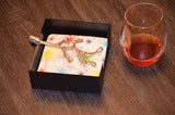 Silver branch-shaped napkin holder with colorful star-patterned napkins inside a black square base, placed next to a glass with amber liquid on a wooden surface.
