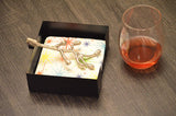 Silver branch-shaped napkin holder resting on colorful star-patterned napkins inside a black square tray, next to a glass with red liquid on a dark wood surface.