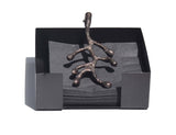 Rectangular matte black napkin holder containing folded black napkins and topped with an antique bronze branching twig-shaped handle.