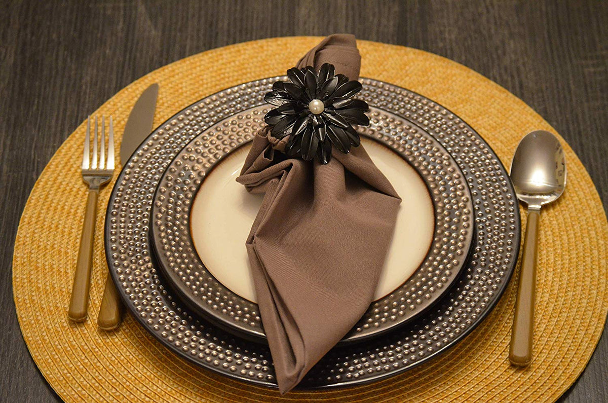 Set of four black floral napkin rings with pearl centers arranged on a neutral fabric