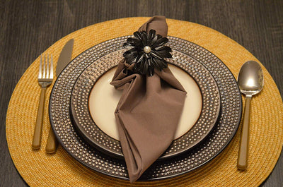 Set of four black floral napkin rings with pearl centers arranged on a neutral fabric