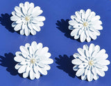 Set of four white floral napkin rings with layered petal design and central pearl-like beads, arranged on a vibrant blue surface casting shadows.