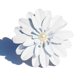 White floral napkin ring with layered petals and a central pearl-like bead casting a shadow on a white background