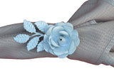 White resin rose napkin ring with detailed petals and leaves, securing a textured beige cloth napkin folded beneath it.