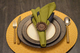 Table setting with cream and dark patterned plates on a yellow woven placemat, featuring green and dark napkins secured by a brown sunflower-shaped napkin ring.