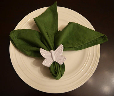 Vibhsa Butterfly White Napkin Rings Set of 4 displayed around folded white napkins on a wooden surface