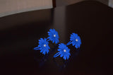 Set of four blue floral napkin rings each shaped like a flower with a white pearl center, placed on a dark polished surface.