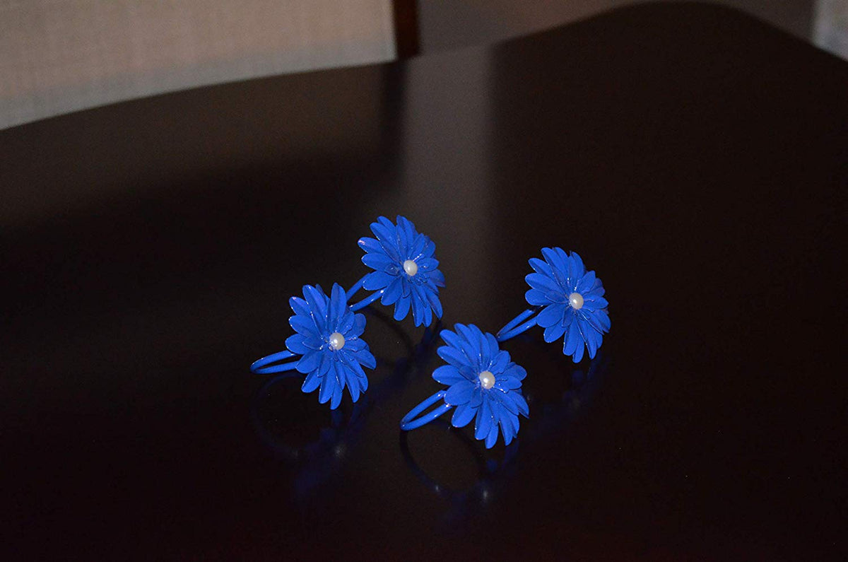 Set of four blue floral napkin rings each shaped like a flower with a white pearl center, placed on a dark polished surface.