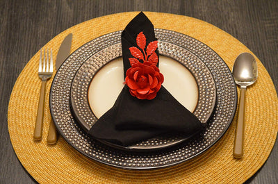 Set of four red rose napkin rings arranged on a dark wood surface.