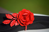 Bright red metal rose with detailed petals and leaves attached as a decorative napkin ring around a black cloth napkin.