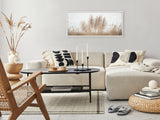 Neutral-toned living room with beige sectional sofa adorned with black-and-white patterned pillows, a wooden woven chair, round woven ottoman, and black coffee table with candles.