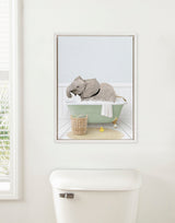 Framed canvas of a baby elephant lying in a pale green clawfoot bathtub with white bubbles, beige rug, small wicker basket, and two yellow rubber ducks in a light blue bathroom.