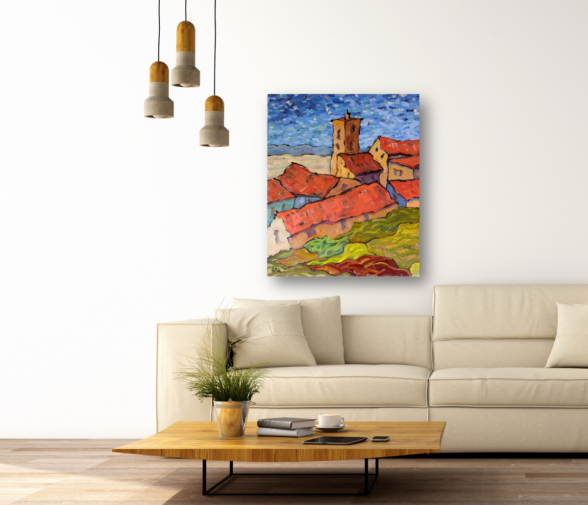 Impressionist-style painting of a village with red rooftops and a tower under a blue sky, hung above a beige sofa in a modern living room.