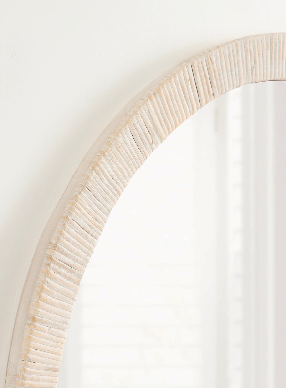 Close-up of a round wall mirror with a textured, off-white ribbed frame showing vertical grooves and subtle horizontal bands near the edge.