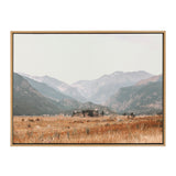 Framed canvas print of a misty mountain landscape with layered peaks and a golden-brown grassy field in the foreground under a pale sky.