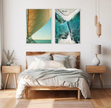 Bedroom with wooden bed and side tables, featuring two framed ocean-themed canvases with sail detail and aerial beach view above the headboard.
