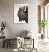 Framed monochrome canvas of a bison's left profile with textured fur and prominent horn, displayed above a woven bench in a sunlit room with wood and plant accents.