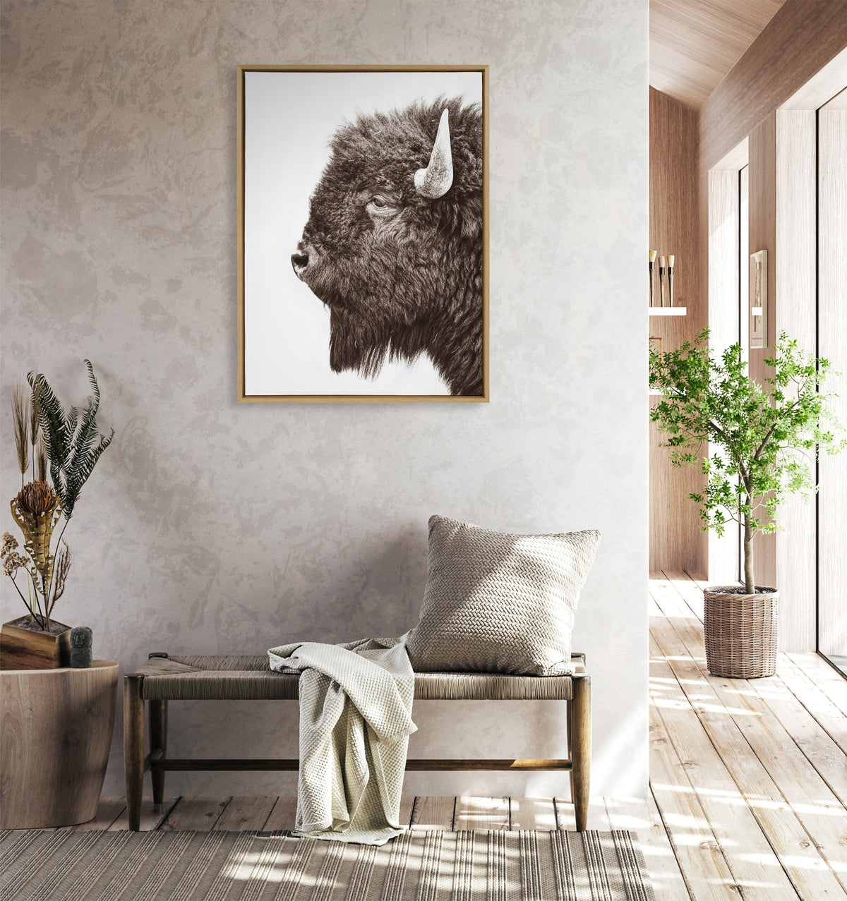 Framed monochrome canvas of a bison's left profile with textured fur and prominent horn, displayed above a woven bench in a sunlit room with wood and plant accents.