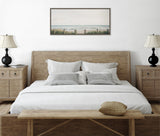 Minimalist bedroom with a natural wood bed frame, white bedding, patterned gray pillows, two matching wood nightstands with black lamps, and a coastal landscape print above the headboard.