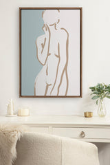Minimalist line art of a nude female figure in tan and teal tones, framed and hung above a white desk with light decor accents.
