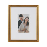 Rectangular wall picture frame with a gold-tone molded border and white mat showcasing a portrait of a smiling couple holding a floral bouquet.