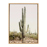 Tall saguaro cactus with five arms standing in desert landscape under pale sky, framed in light wood with sparse bushes and smaller cacti in background.