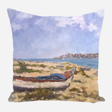 Pillow with painted scene of a weathered boat on sandy beach under a partly cloudy blue sky, distant town and sea in the background.