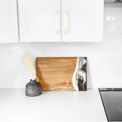 acacia resin serving bread board with a vase and abstract art on a kitchen counter.