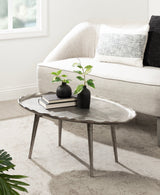 Oval coffee table with a textured gray metal surface and scalloped edges, supported by four angled metal legs, styled with two small black vases and books