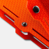 Close-up of a bright orange material with a honeycomb pattern, featuring two metal rivets and precise angular cutouts on its layered structure.