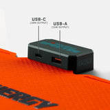 Black rectangular adapter with labeled USB-C (18W) and USB-A (15W) ports resting on textured orange material with partial word 'ENERGY' visible.
