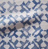 Close-up of a textured fabric pillow cover with an indigo blue geometric pattern on a beige background, showing interlocking rectangular shapes.