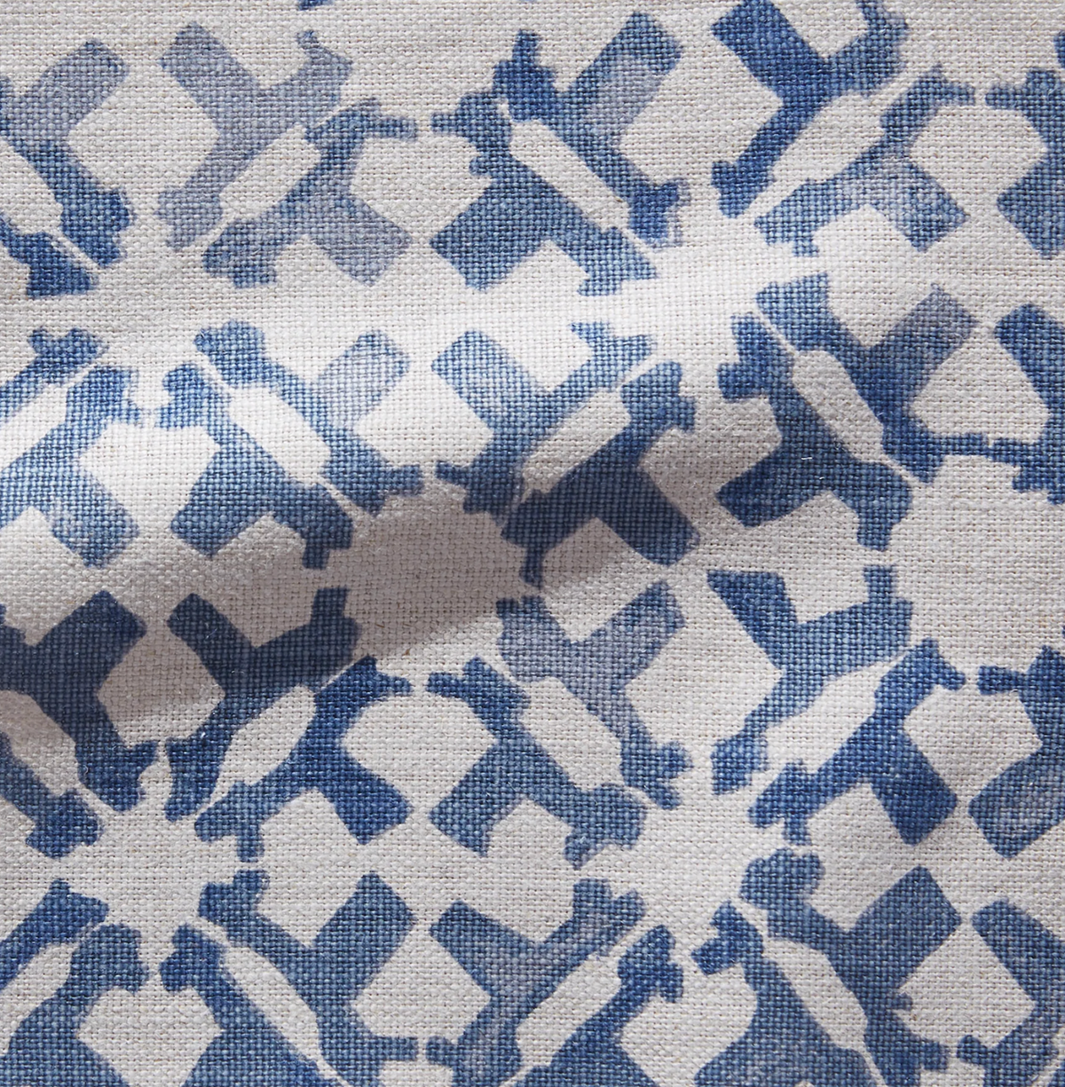 Close-up of a textured fabric pillow cover with an indigo blue geometric pattern on a beige background, showing interlocking rectangular shapes.