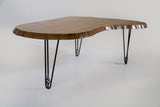 Kidney-shaped wooden table with wavy live edges and glossy finish, supported by three black hairpin legs with geometric detail.