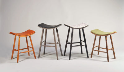 EB Saddle Stools with turned wood legs and saddle-shaped seats upholstered in various materials
