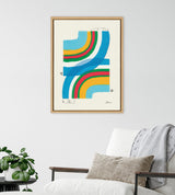 Abstract artwork with overlapping curved bands in blue, green, yellow, orange, and red on a cream background, framed in light wood and hanging above a chair with neutral pillows.