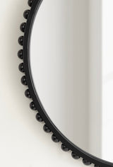 Close-up of a round wall mirror with a black frame embellished by evenly spaced black spherical beads along its edge, against a white background.