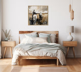 Neutral-toned abstract painting of two horseback riders viewed from behind, hanging above a minimalist bed with wooden headboard and soft blue-gray bedding.