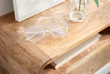 Close-up of light brown wooden side table corner with smooth rounded edge, showing clear eyeglasses and glass vase with a green leaf on top