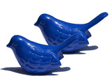 Two small blue bird figurines with detailed feather patterns and raised tails casting shadows on a white background.
