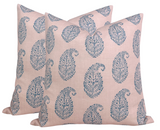 Two square pillow covers in soft pink fabric patterned with repeating blue paisley motifs featuring intricate leaf-like details.