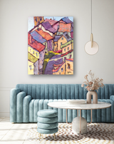 Abstract painting of colorful houses with red, orange, and yellow roofs viewed from above, hanging above a teal velvet sofa in a modern living room.