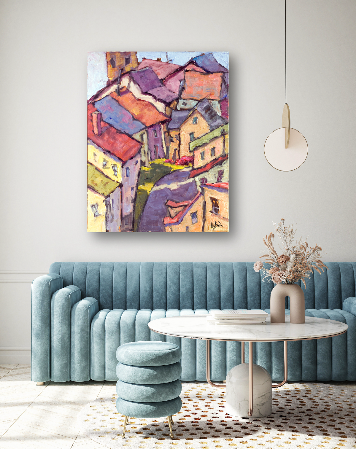 Abstract painting of colorful houses with red, orange, and yellow roofs viewed from above, hanging above a teal velvet sofa in a modern living room.