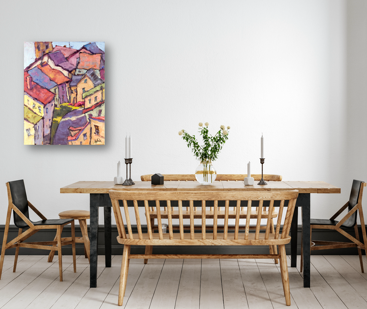 Dining room with wooden table and chairs, featuring a vase with white flowers and two tall candlesticks, wall-mounted colorful abstract cityscape painting.