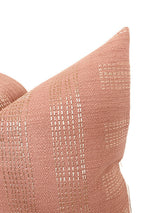 Close-up of a square pillow cover in muted rose with subtle ivory stitched linear and rounded pattern details against a white background.