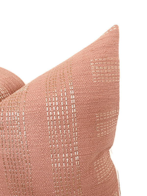 Close-up of a square pillow cover in muted rose with subtle ivory stitched linear and rounded pattern details against a white background.