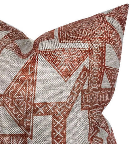 Close-up of a pillow corner with an orange geometric tribal pattern on textured beige fabric.